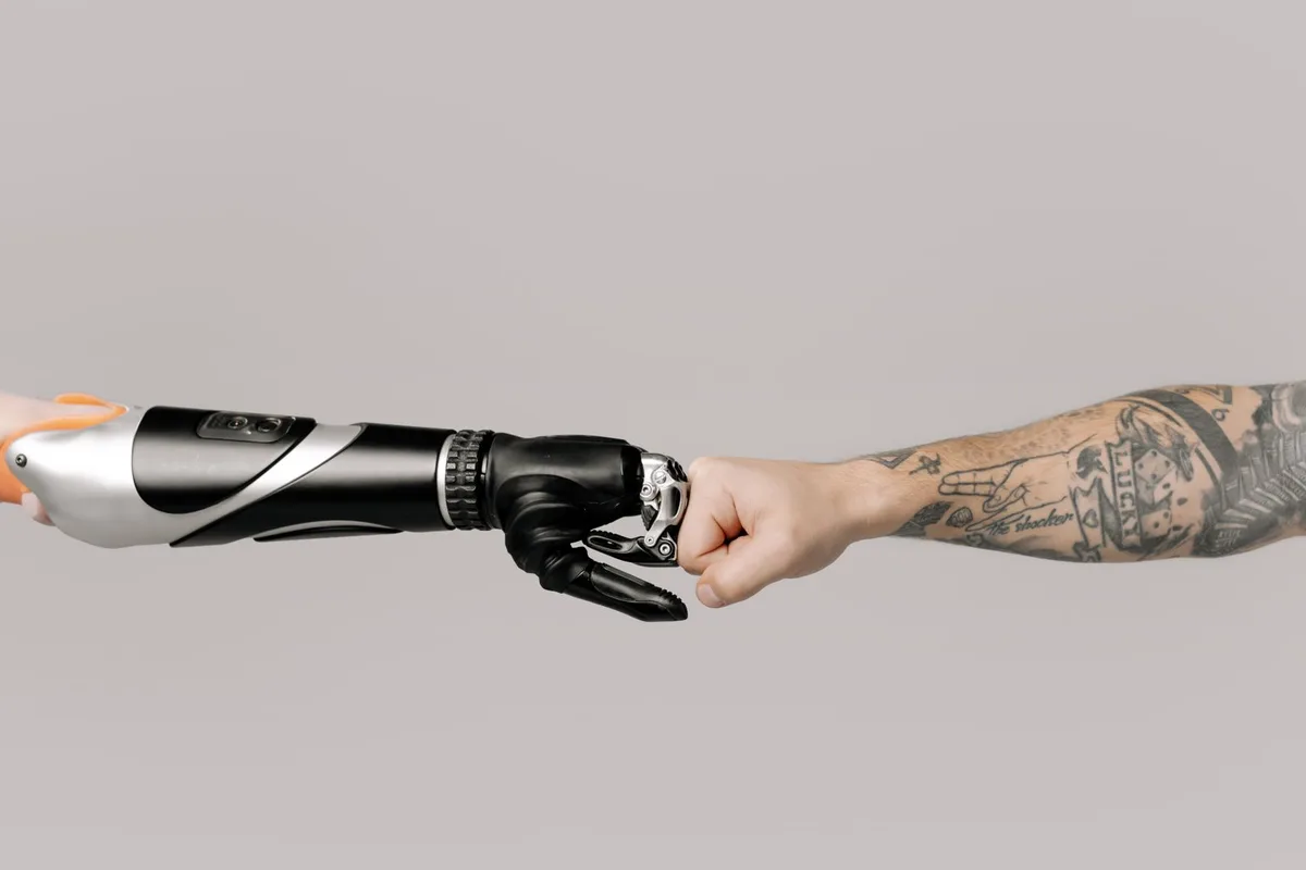 Fist bump between a tattooed arm and a robotic arm