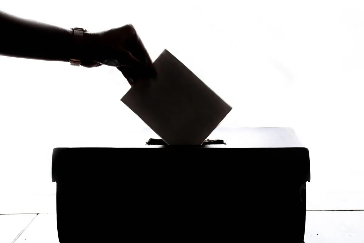 Silhouette of a hand placing a vote into a ballot box