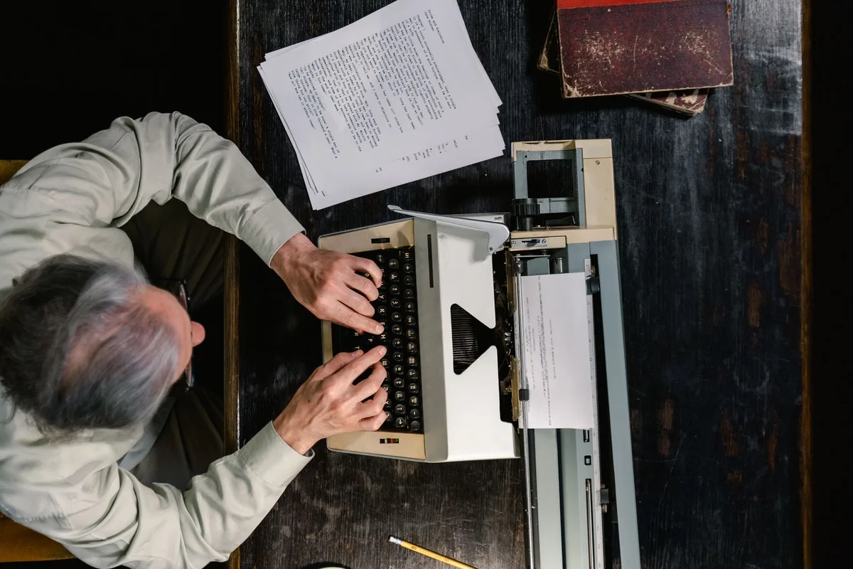 Person typing on a vintage typewriter, scattered papers