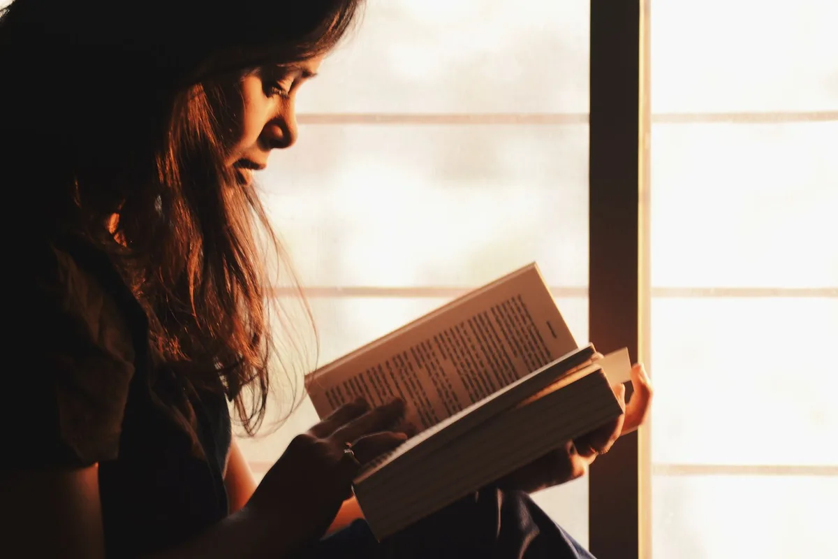 A woman engrossed in a book by a sunlit window