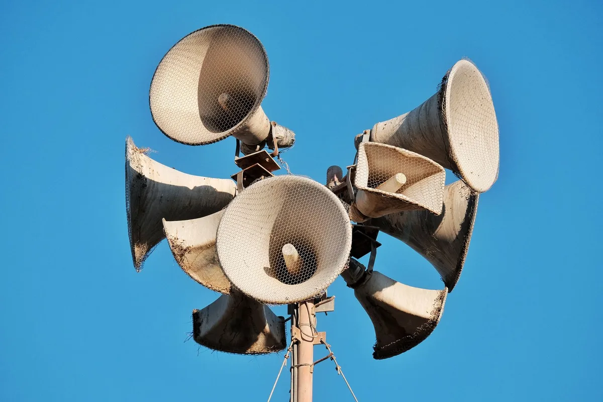 Aged megaphones on a pole against a clear blue sky