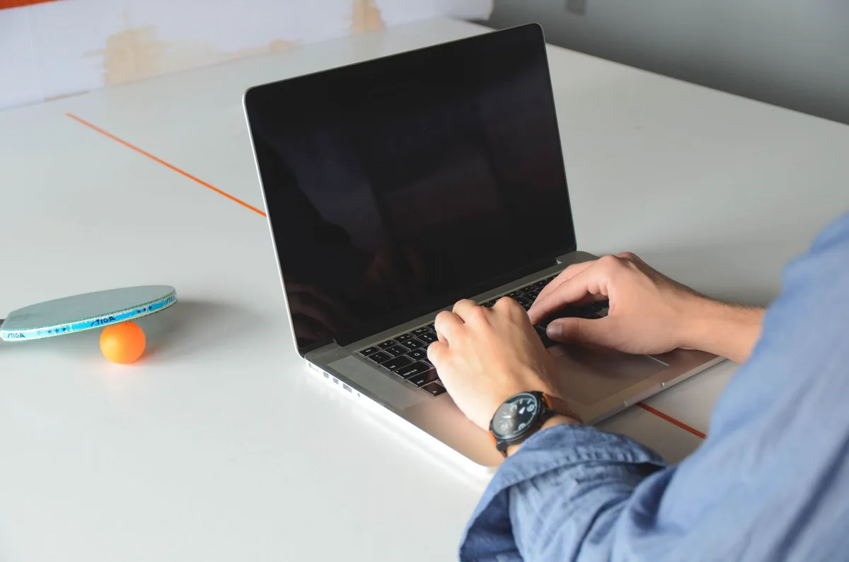 Person typing on a laptop, ping pong paddle nearby