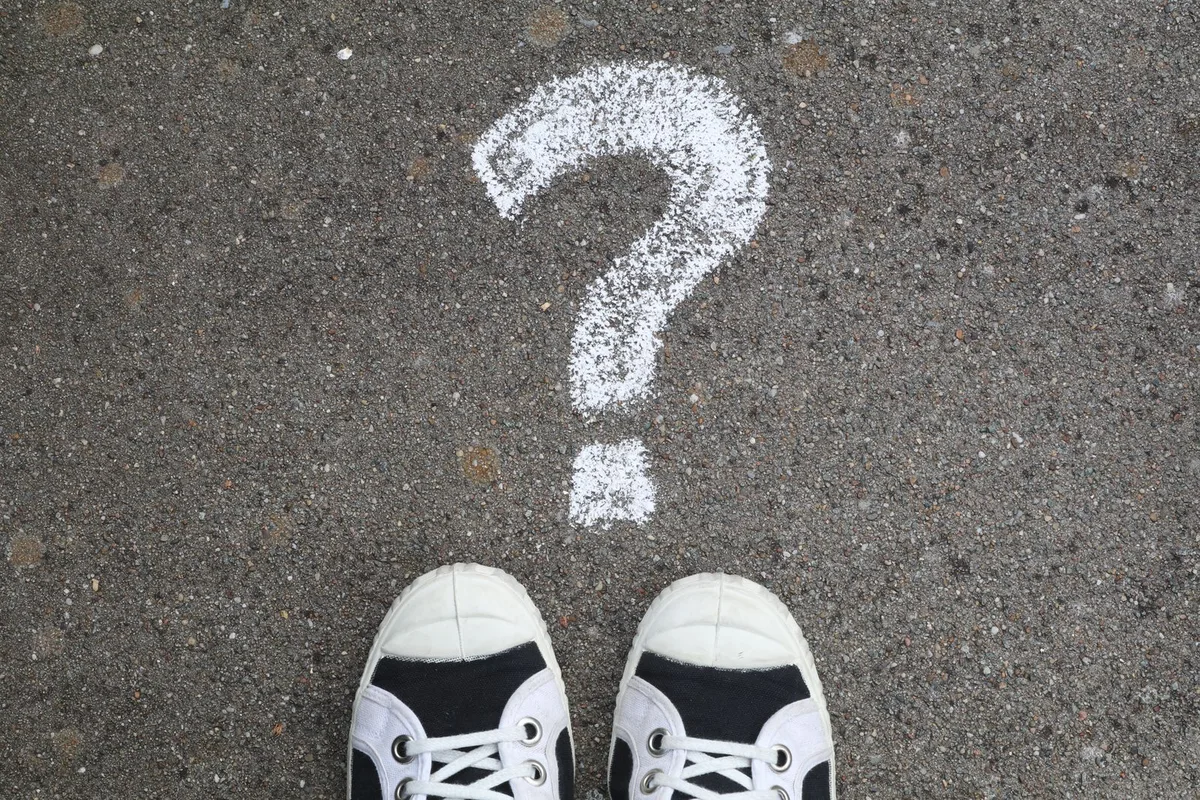 Sneakers on pavement with a chalk question mark